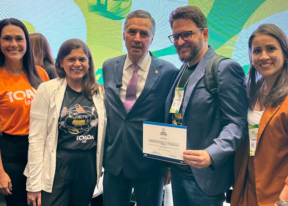 Grupo de cinco pessoas lado a lado, em foto parcial, com o ministro Luis Roberto Barroso ao centro, e o juiz Felipe Damous ao seu lado exibindo um cerificado. Há Mais três mulheres ao lado deles