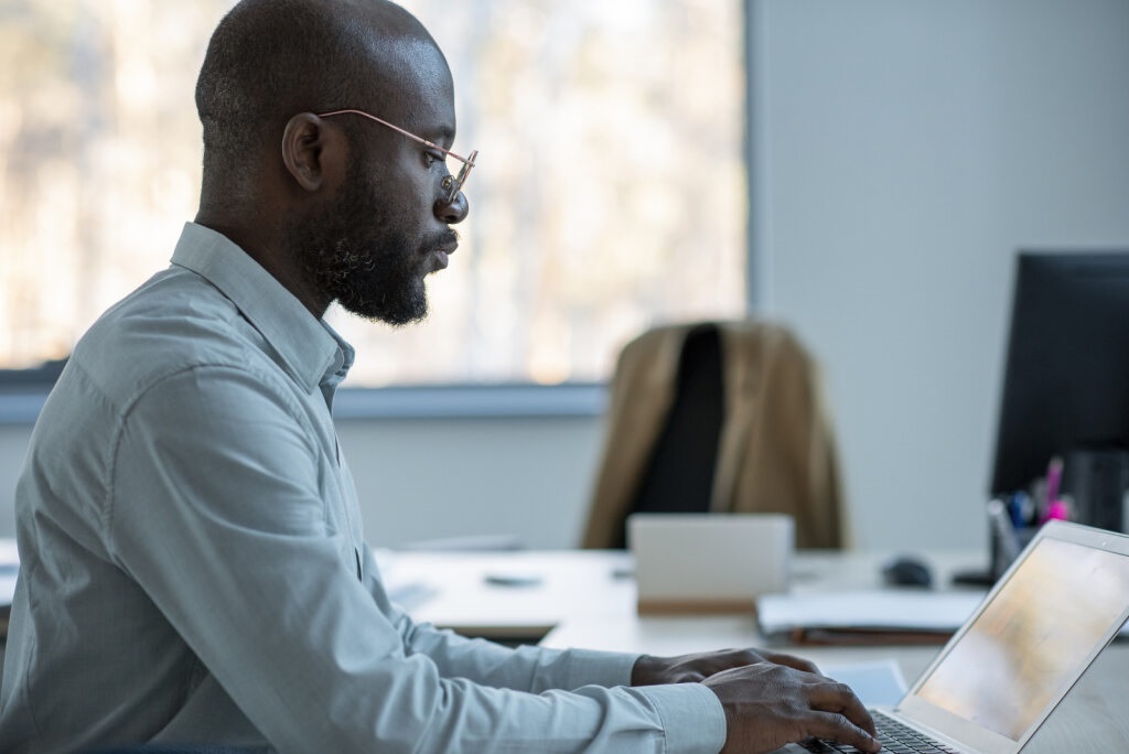Homem negro de perfil digita em notebook