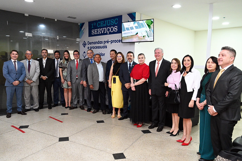 A imagem mostra um grupo de pessoas em fila para uma oportunidade de foto. Elas estão em um ambiente interno, e os rostos de todos os indivíduos foram ocultados com retângulos marrons para preservar a privacidade. Ao fundo, há uma faixa com texto em português, que parece estar relacionada a um evento ou instituição chamada ¿1º CEJUSC SERVIÇOS¿