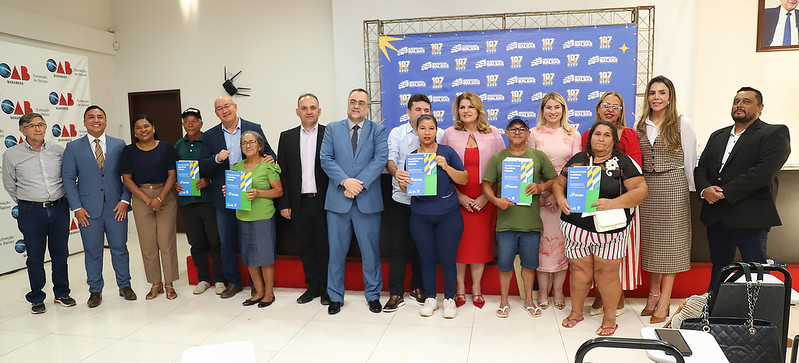 Foto horizontal: TJMA e Prefeitura de Balsas entregam 50 títulos de propriedade. A imagem mostra um grande grupo de pessoas posando para uma foto em um evento. A maioria está em pé, e alguns seguram documentos.