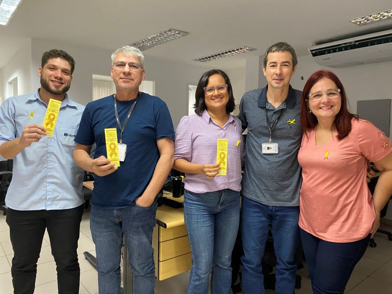 Foto colorida mostra 5 pessoas em pé segurando marcadores de livros e sorrindo, durante ação do Setembro Amarelo. São 3 homens e duas mulheres.