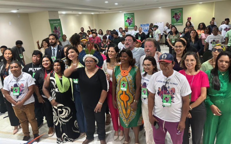 Foto horizontal de evento em que o Núcleo de Governança Fundiária do TJMA participa de Oficina de Governança em Terras Indígenas. A imagem mostra um grupo de pessoas reunidas em uma sala para reunião. As pessoas estão em várias fileiras e algumas estão usando crachás. Ao fundo, há um banner com textos e logotipos, que mostram que o evento é relacionado às questões indígenas.