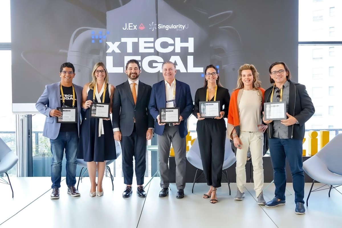 Foto horizontal de evento com participação do TJMA, o xTech Legal. A imagem mostra um grupo de sete pessoas em frente a um painel com o texto "JEX xTech Legal". Cinco pessoas estão segurando um certificado. Todos estão vestidos com trajes formais. O painel mostra que é um evento relacionado à tecnologia jurídica, organizada pela JEX em colaboração com a Singularity University.