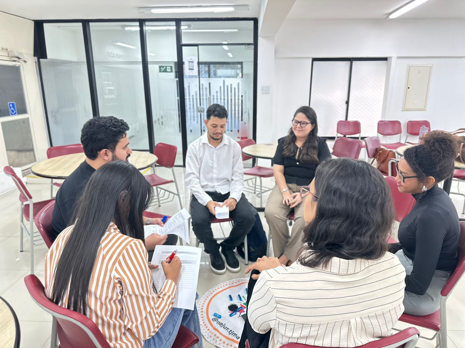 grupo de pessoas sentadas em formato circular e ambiente interno durante atividade restaurativa