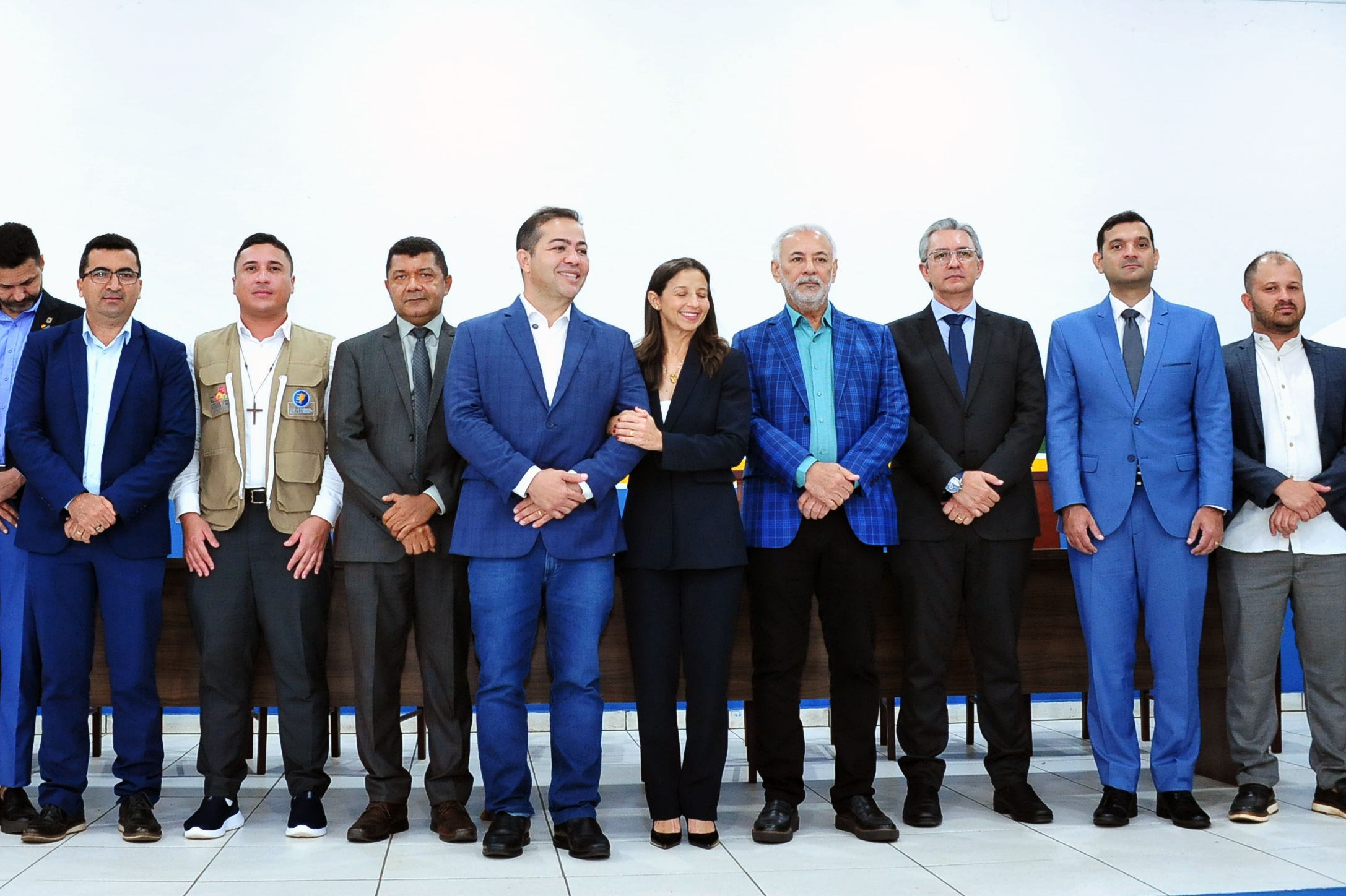 Imagem mostra autoridades alinhadas à frente da mesa de honra para fotografia oficial. Todos estão de pé, lado a lado, vestidos em trajes formais. No centro, o prefeito Rildo Amaral e a vice-prefeita concentram olhares e sorrisos. O grupo reúne representantes do Executivo, Judiciário e SERF. O ambiente é iluminado e tem fundo branco.