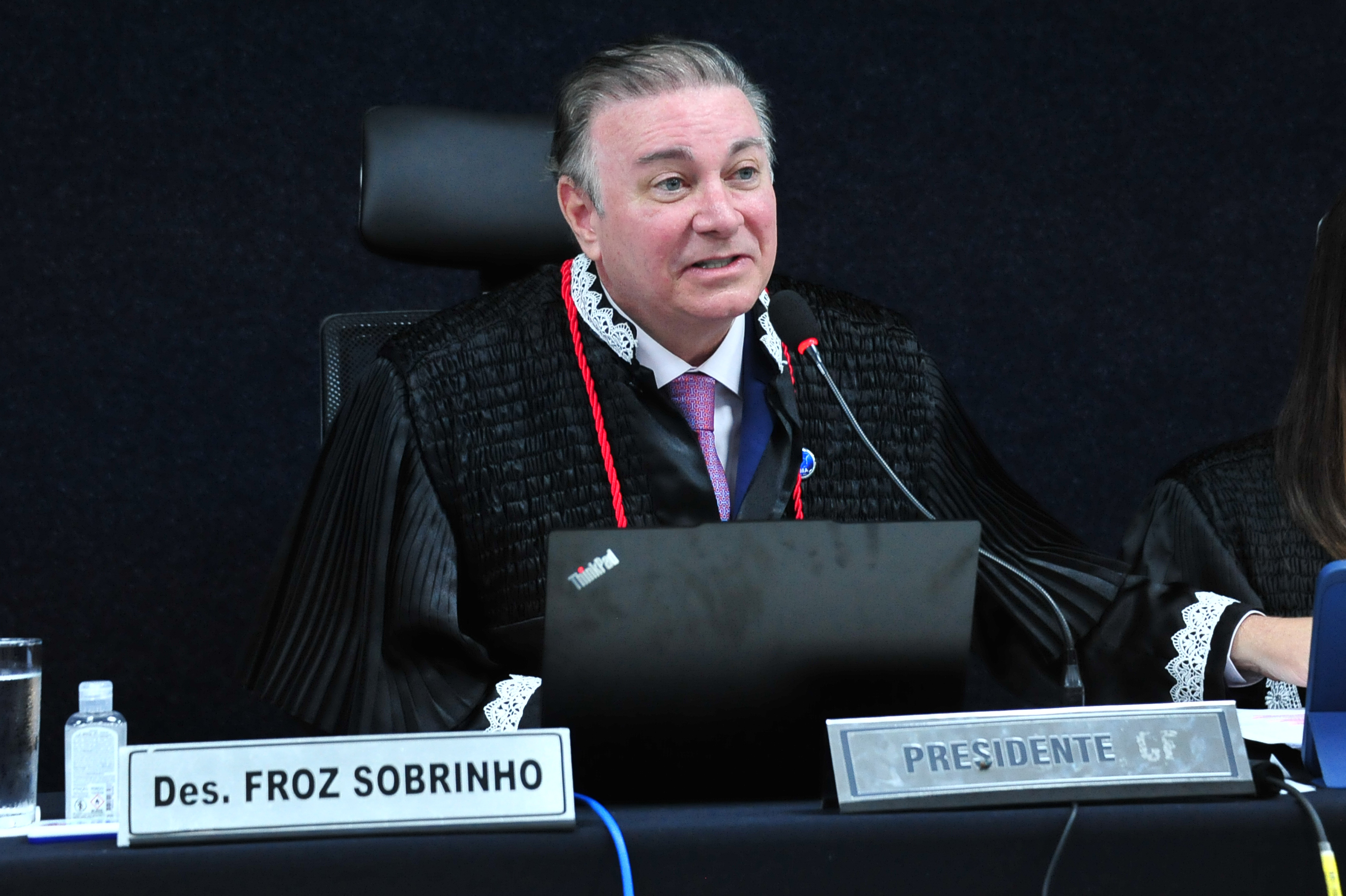 Esta imagem é um close-up que foca no Desembargador Froz Sobrinho, que aparece sentado e falando durante a sessão formal.