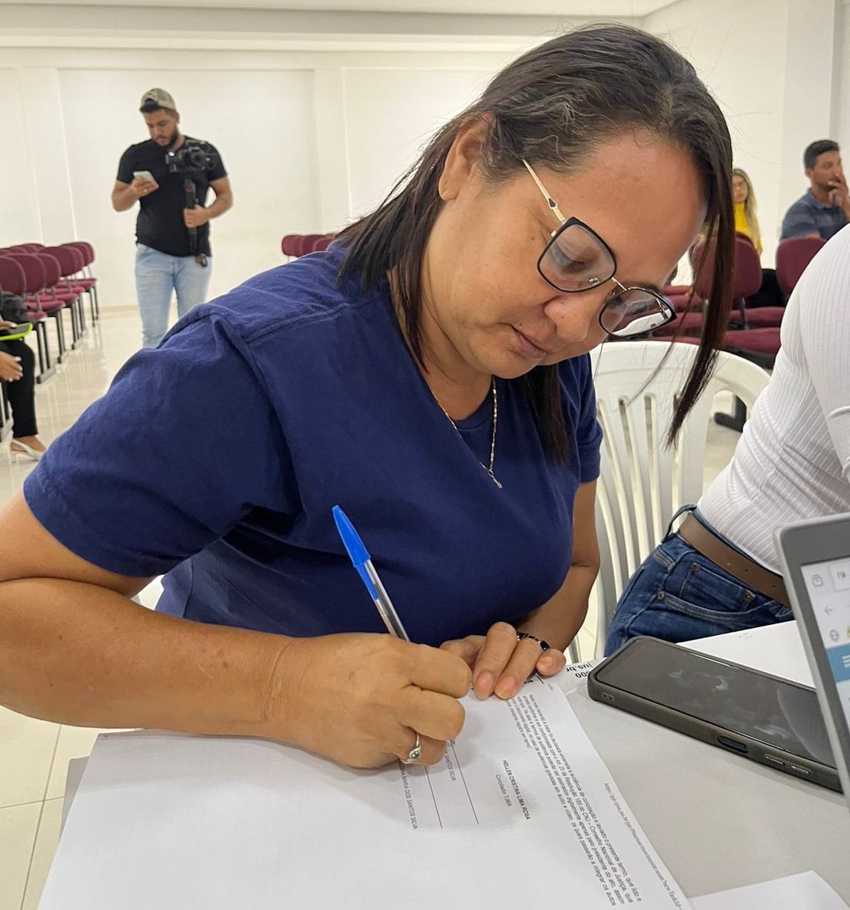 Foto colorida mostra uma senhora sentada assinando um documento, um termo de acordo, durante audiência no evento Conciliação Itinerante, em Grajaú.