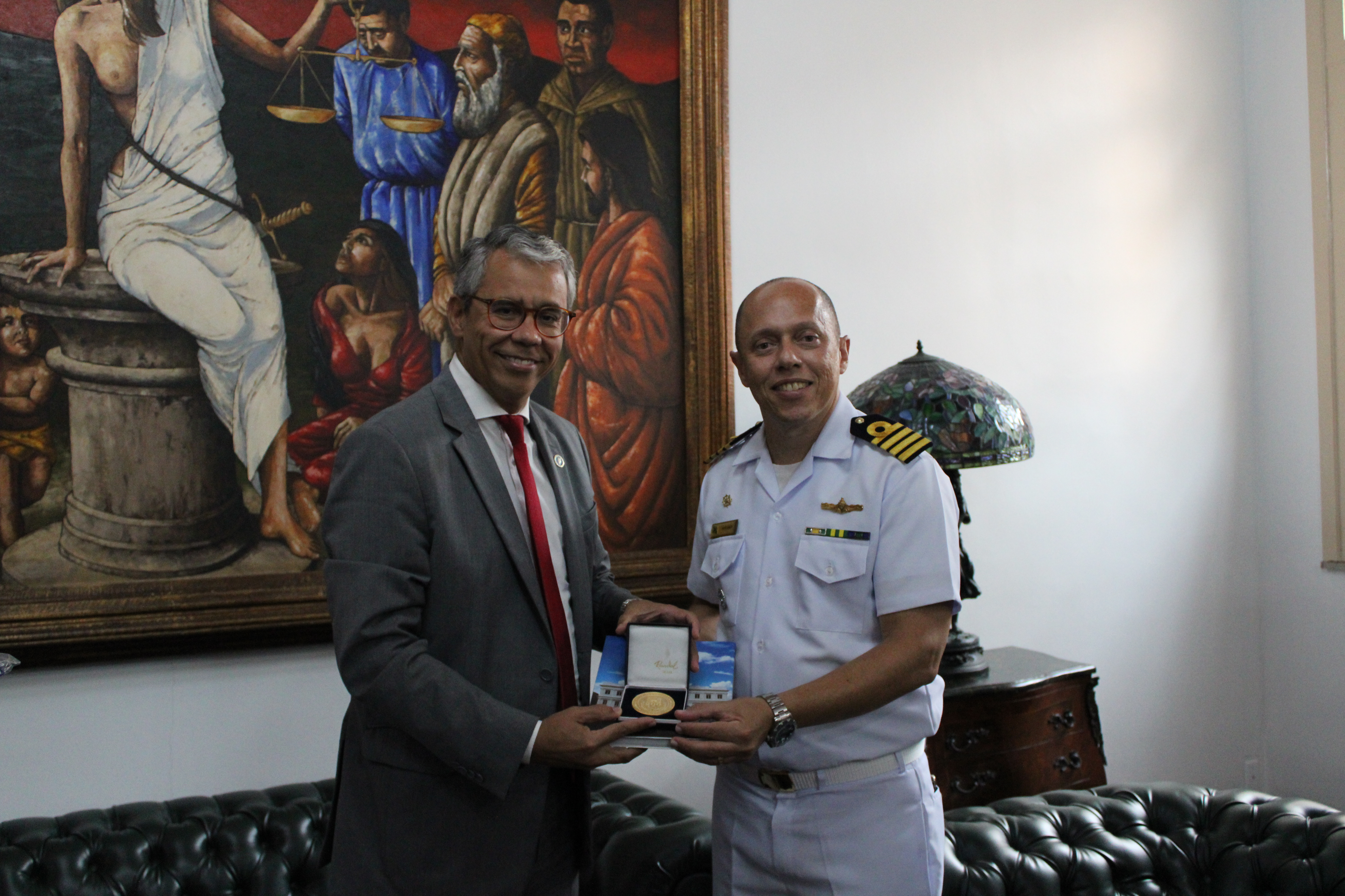 O Capitão dos Portos de farda recebendo livro e medalha do TJMA das mãos do presidente do TJMA, desembargador Paulo Velten. Os dois em pé e sorrindo