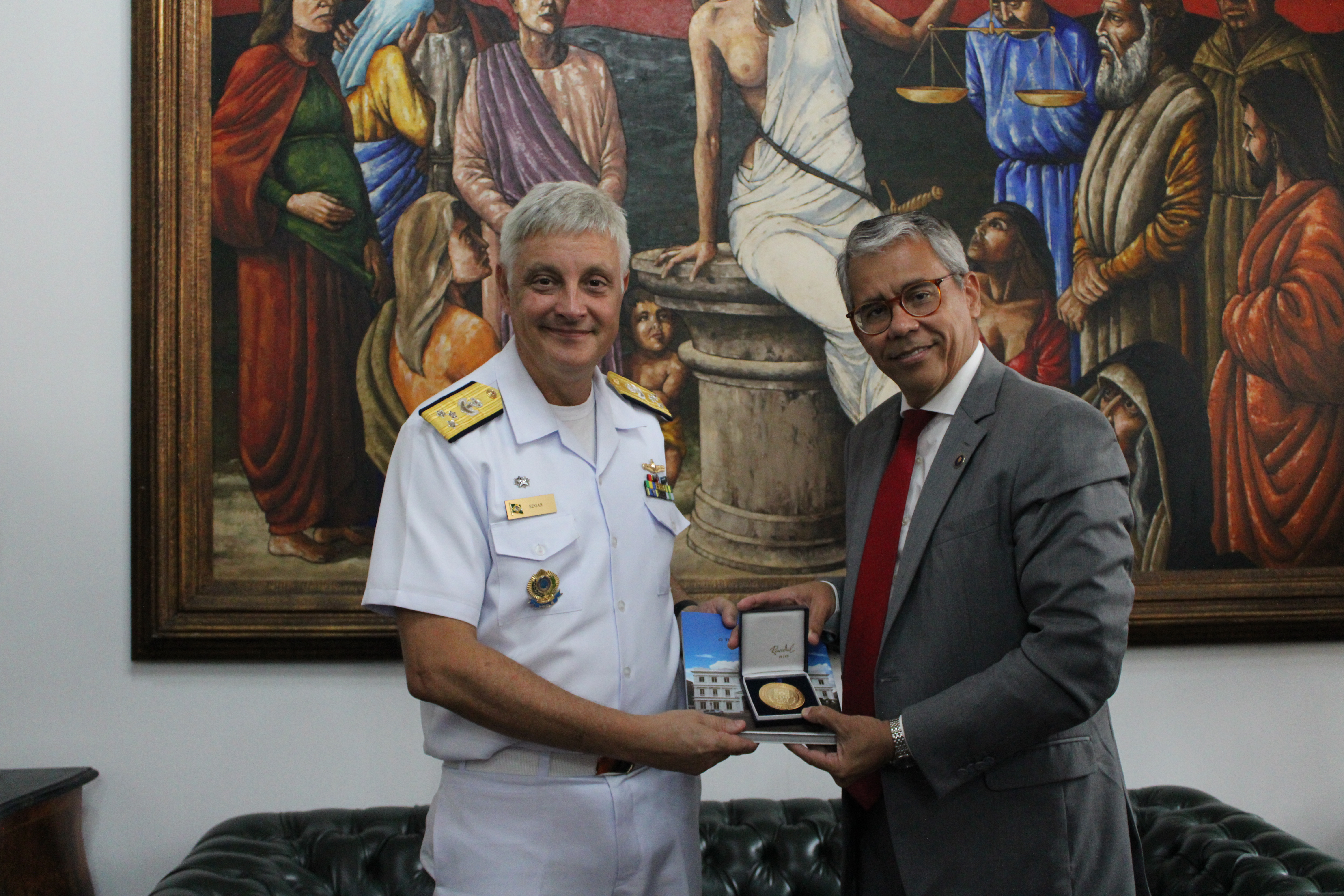O vice-lamirante de farda recebendo um livro e medalha do TJMA das mãos do presidente do TJMA de terno em pé
