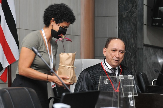 Presidente do TJMA, desembargador Lourival Serejo, recebe muda de planta em sessão plenária. Ele está sentado à mesa da presidência na sala das sessões plenárias.