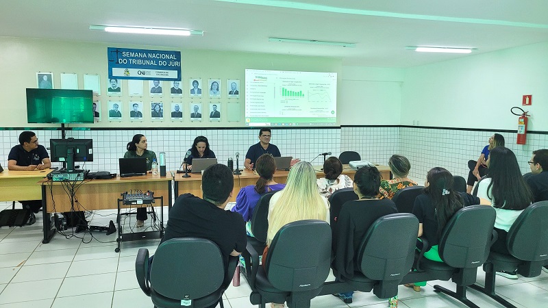 pessoas sentadas aparecem de costas atentas as explicacoes de um homem sentado à frente de um notebook