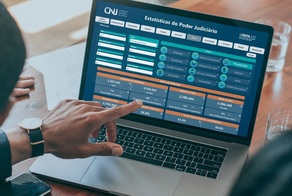 Pessoa aponta para tela de computador. Na tela um sistema de cadastros de processos previdenciários.