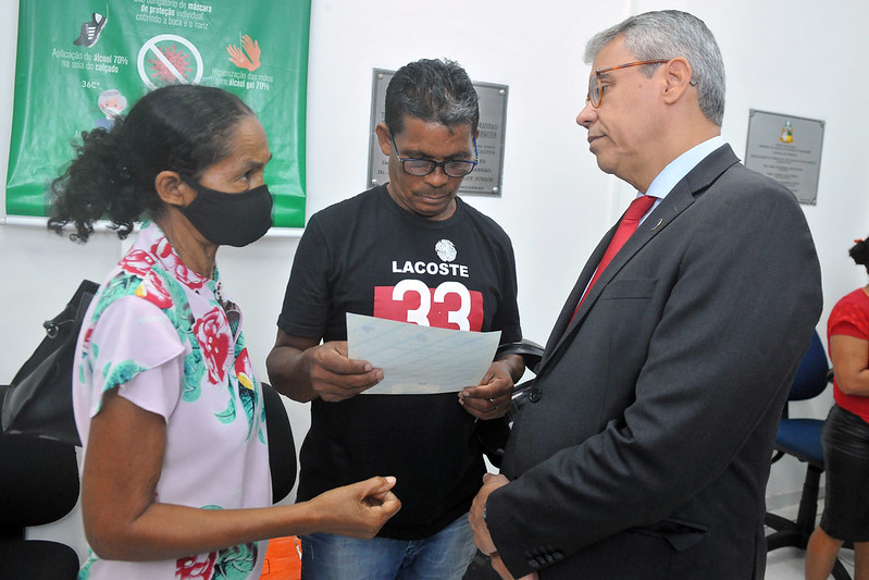 Foto colorida. Presidente do TJMA, conversa frente a frente com uma senhora da comunidade, ao lado de um homem que lê um documento de registro civil