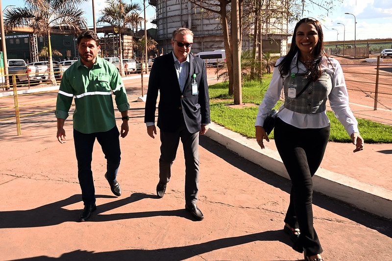 Em ambiente externo, desembargador Froz Sobrinho, juiza Ana Beatriz Maia e advogado da empresa AVB caminham. Atrás, maquinários e estruturas grandes de siderurgia