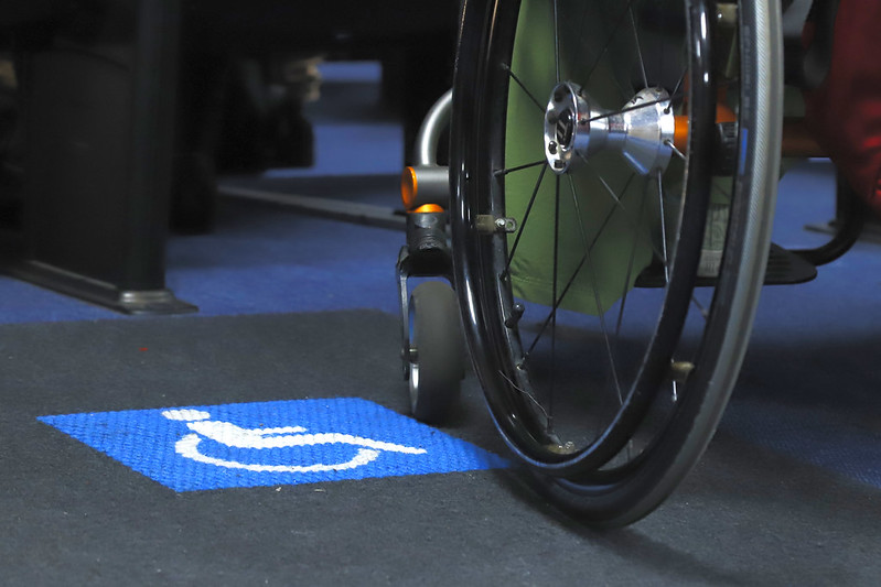 Dia Internacional da Pessoa com Deficiência tem Judiciário engajado na luta anticapacitista imagem de ambiente interno com chao de carpete, onde aparece uma impressão do simbolo das pessoas com deficiencia e parte de uma cadeira de rodas ao lado