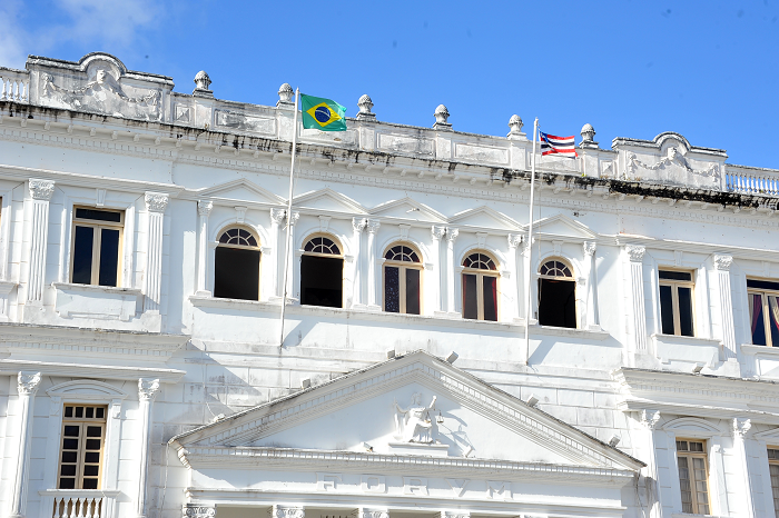 Fotografia diurna da fachada parcial do prédio sede do TJMA, monstrando colunas e bandeiras do Brasil e do Maranhão hasteadas