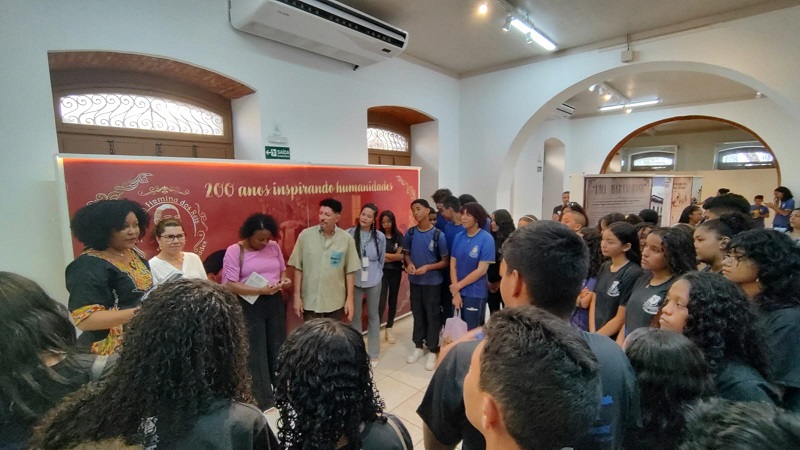 Em ambiente interno, grupo de estudantes observa fala de servidora do TJMA durante encerramento da exposição Maria Firmina