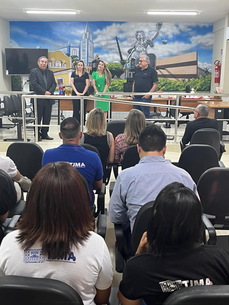 Foto colorida do desembargador junto com a juíza de verde e servidores em pé de frente para servidores que estão sentados no auditório