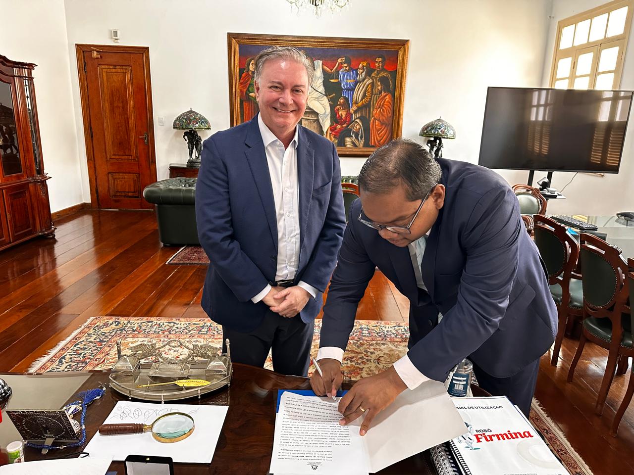 Em ambiente interno, desembargador froz sobrinho e o juiz Marco Adriano Ramos, lado a lado, enquanto o juiz assina um documento