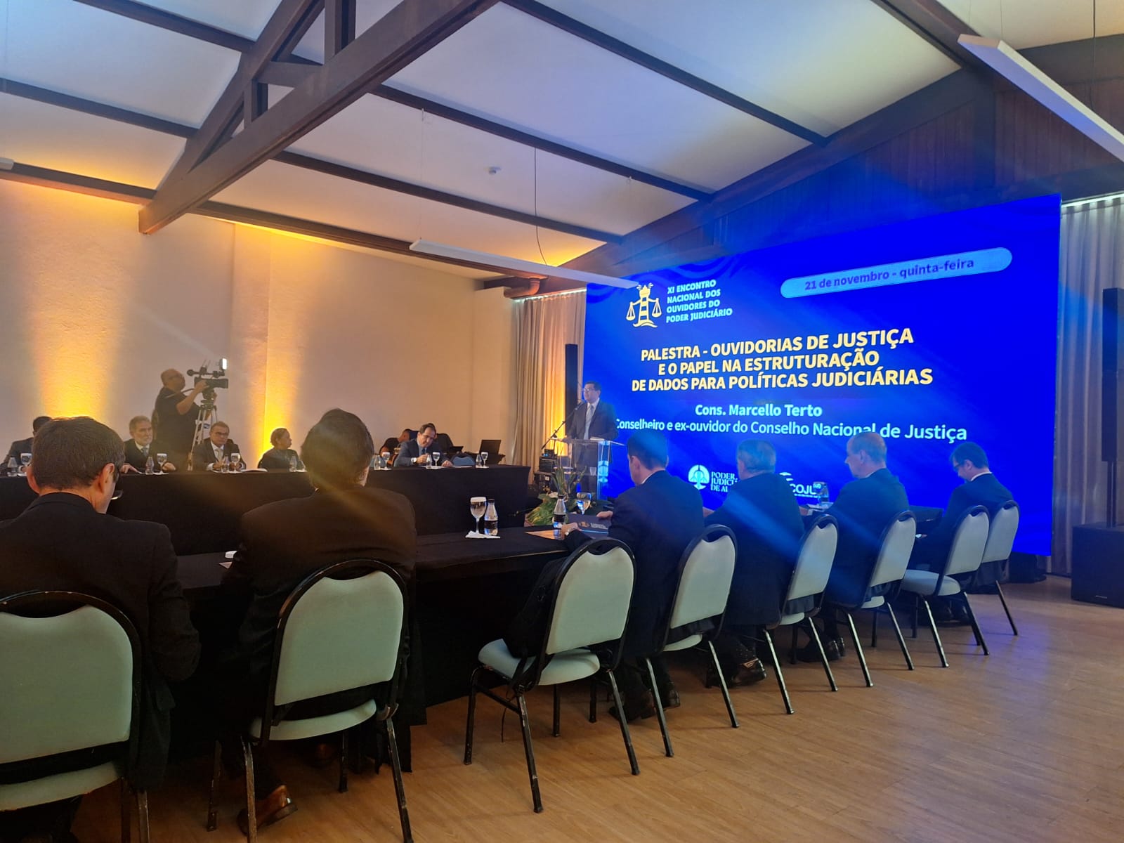 A imagem mostra um evento formal em um salão de conferências. Há várias pessoas sentadas em cadeiras, voltadas para um palco onde um palestrante está falando. No fundo, há um grande painel azul com o seguinte texto:

**"30º ENCONTRO NACIONAL DOS OUVIDORES DO PODER JUDICIÁRIO 21 de novembro - quinta-feira

PALESTRA - OUVIDORIAS DE JUSTIÇA E O PAPEL NA ESTRUTURAÇÃO DE DADOS PARA POLÍTICAS JUDICIÁRIAS Cons. Marcello Terto Conselheiro e ex-ouvidor do Conselho Nacional de Justiça"**

O evento parece ser uma palestra sobre o papel das ouvidorias de justiça na estruturação de dados para políticas judiciárias, ministrada por Marcello Terto, conselheiro e ex-ouvidor do Conselho Nacional de Justiça.