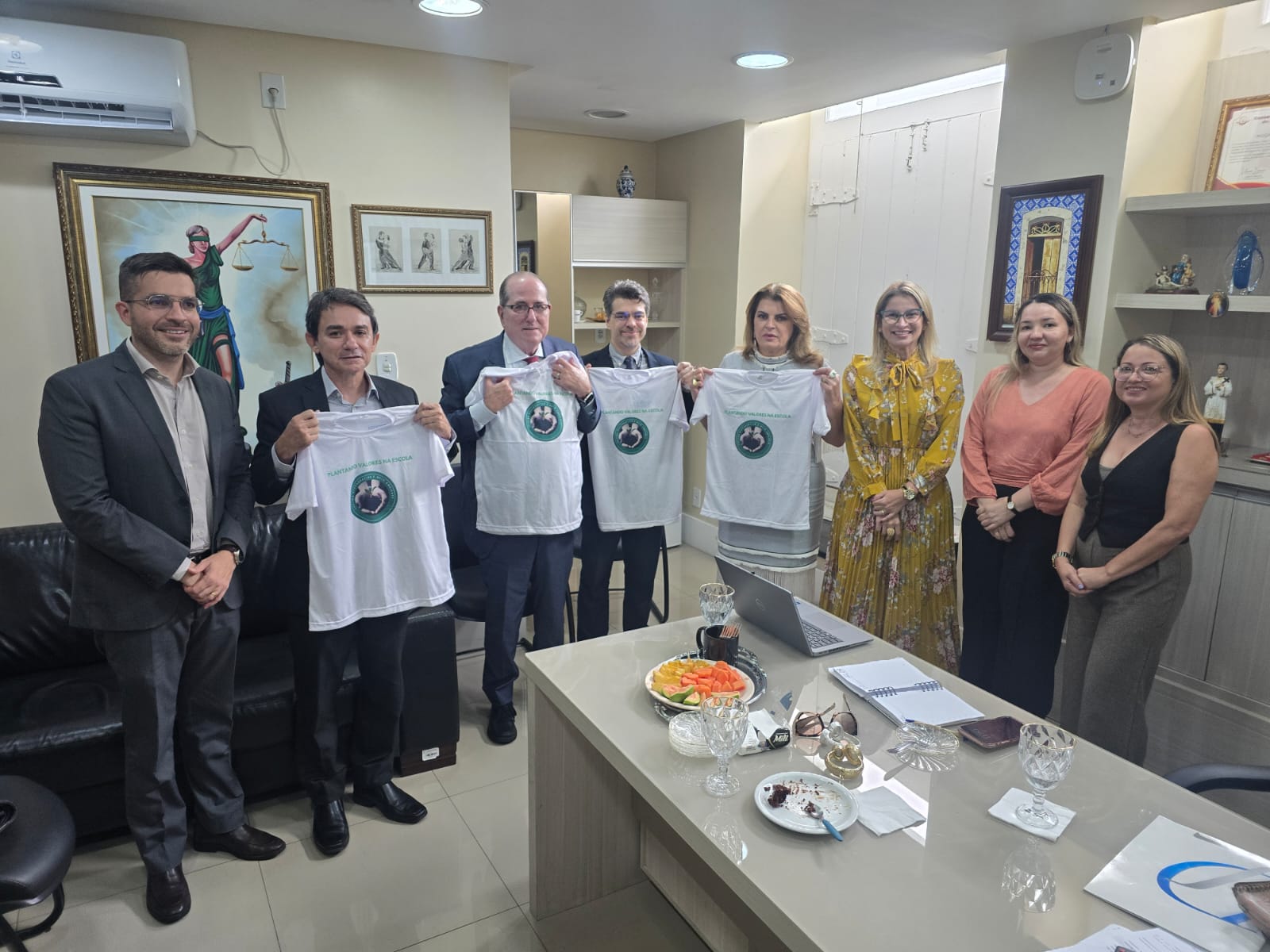 em ambiente interno corporativo, quatro homens e quatro mulheres vestidos formalmente posam para foto, em pé, lado a lado. Quatro deles exibem camisas brancas de projeto