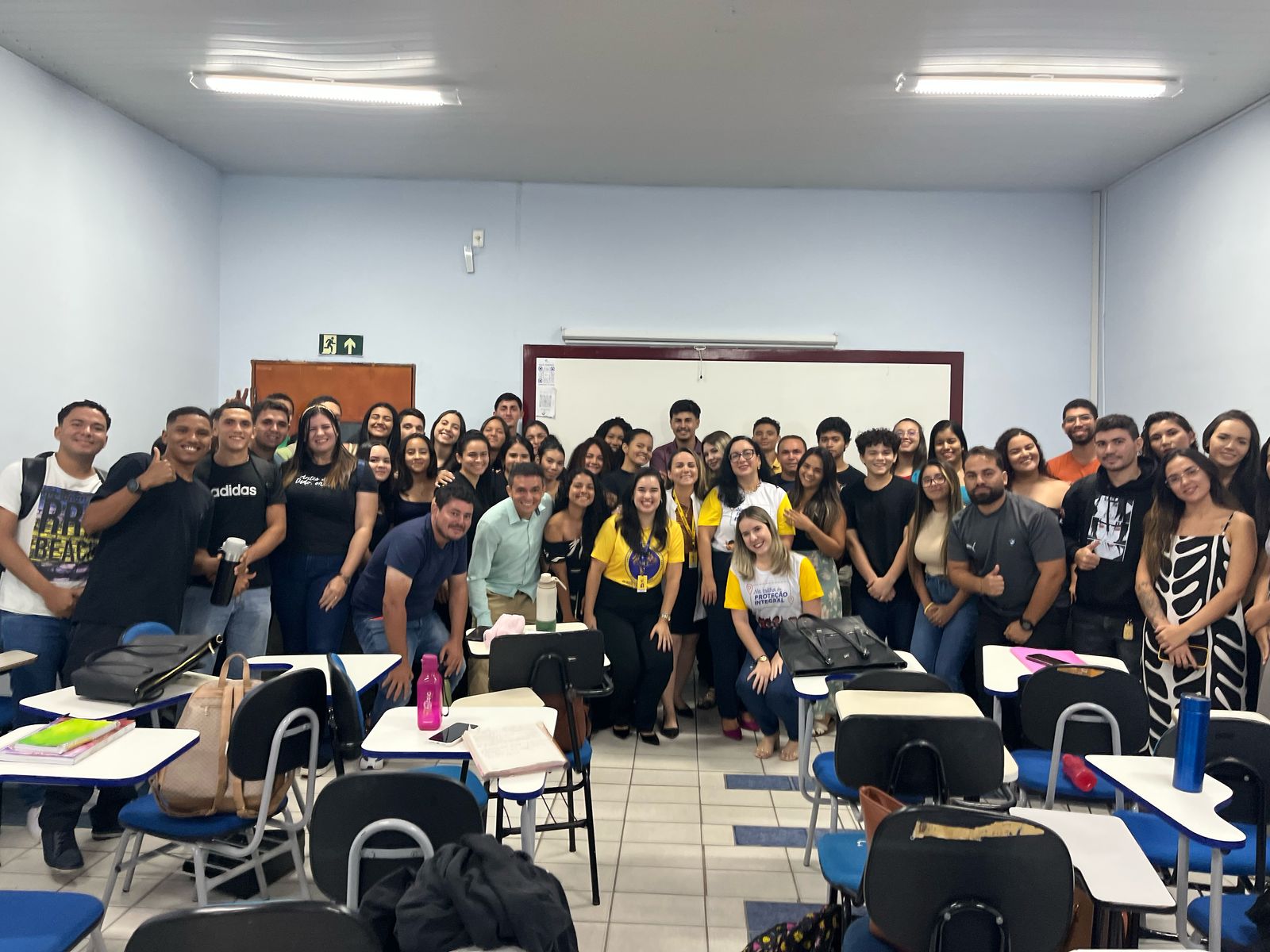 Cerca de 45 pessoas posam para foto, em sala de aula. Elas sorriem. Em frente delas, carteiras, e atrás, quadro branco.
