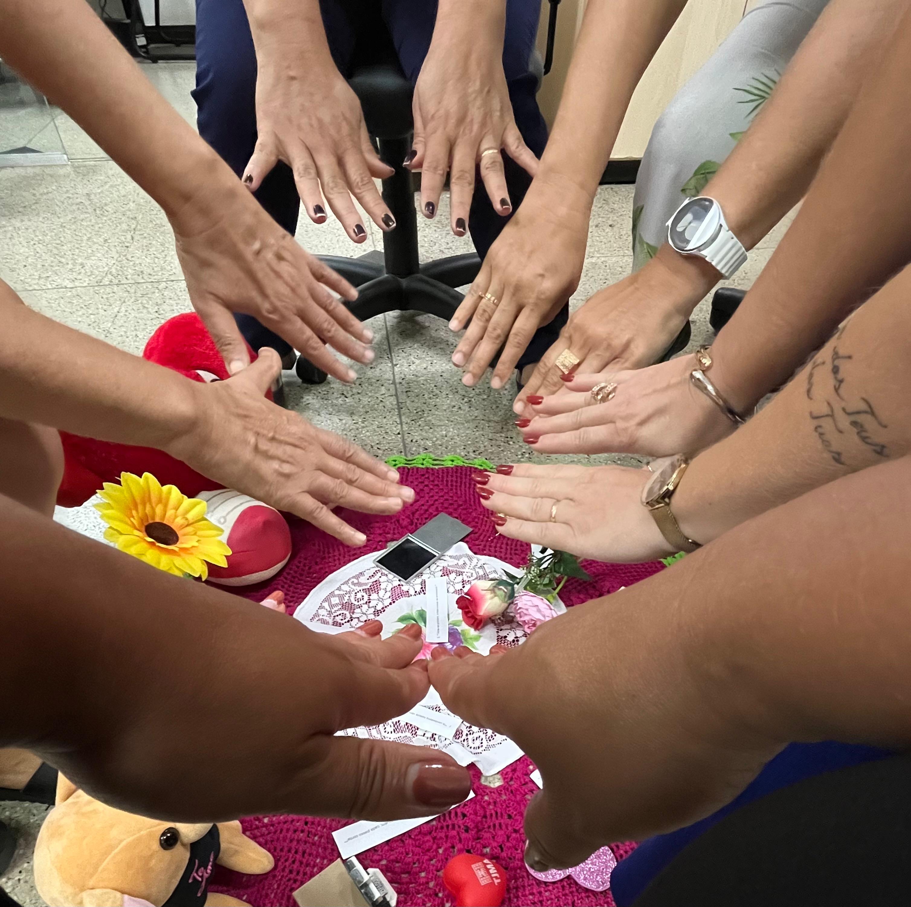 maos humanas dispostas em formato circular sobre uma serie de objetos e tapete de crochê nao chao