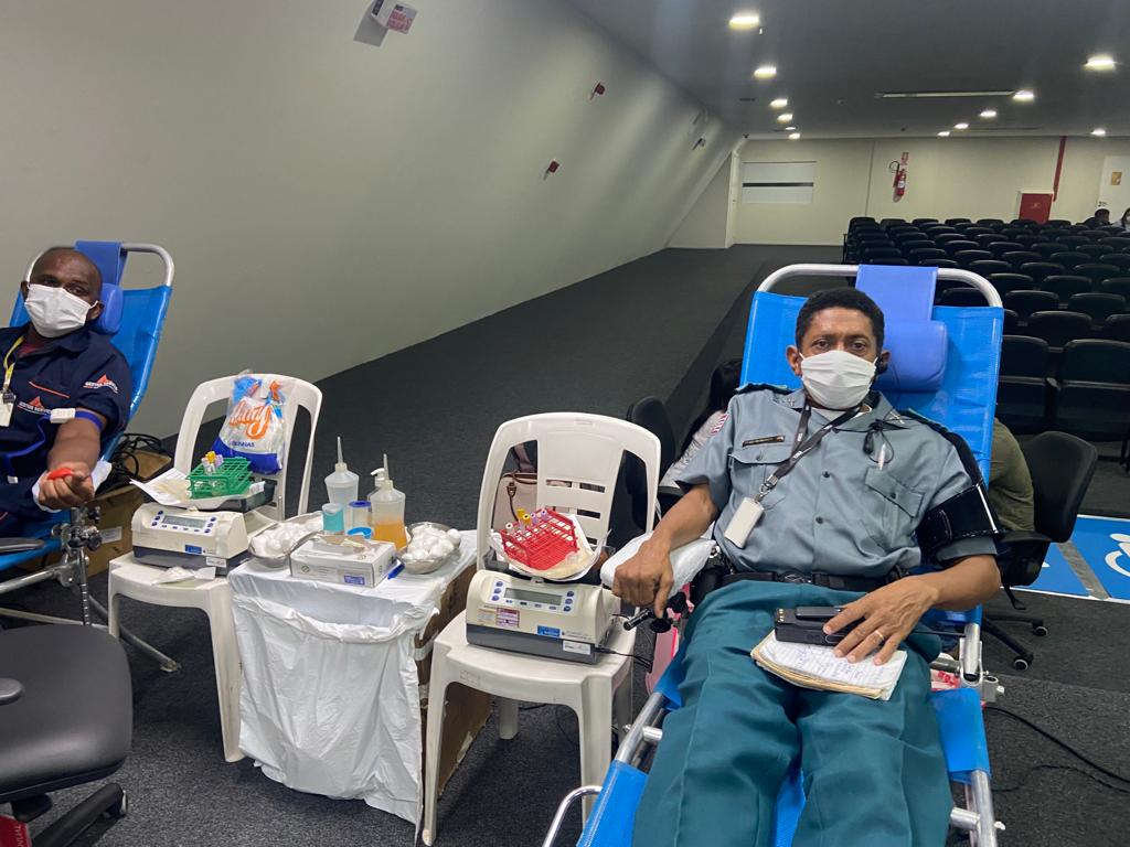 Foto colorida. Funcionários da empresa gestor e militar estão deitados em cadeiras azuis reclináveis enquanto doam sangue.