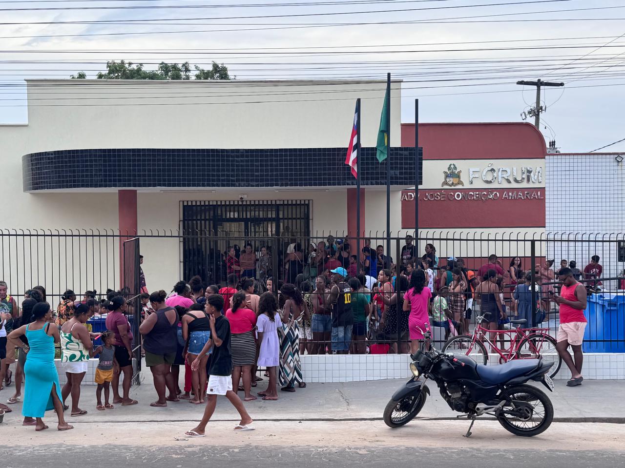 imagem distante de um aglomerado de pessoas. elas estão em frente a um prédio onde funciona um forum