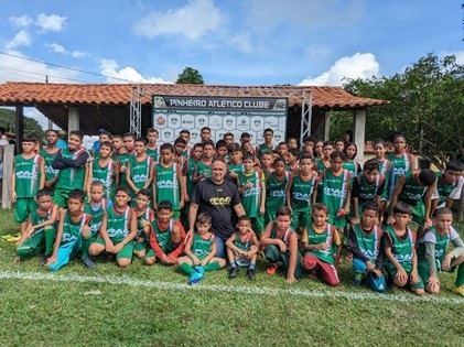 imagem na qual aparecem diversas crianças, em um campo de futebol, posando para a foto, enfileiradas, utilizando uniforme verde