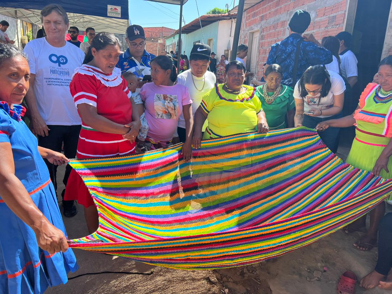 Foto horizontal de homens e mulheres venezuelanas em espaço aberto, abrindo rede nas cores vermelha e verde.