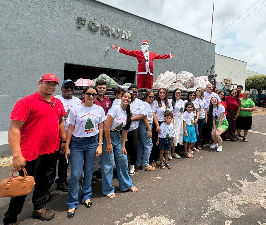 imagem na qual aparecem muitas pessoas na rua. elas estão na frente de um prédio do fórum, . atras delas tem um caminhão com brinquedos em cima e uma pessoa vestida de papai noel