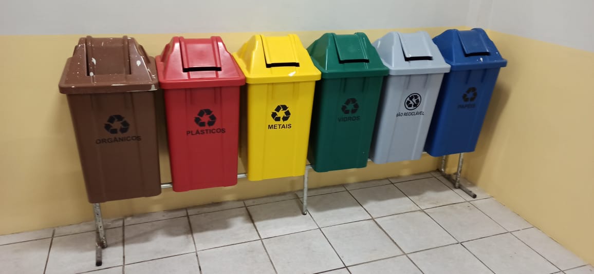 Fileira de lixeiras plásticas nas cores verde, azul, amarela e vermelha instaladas no chão