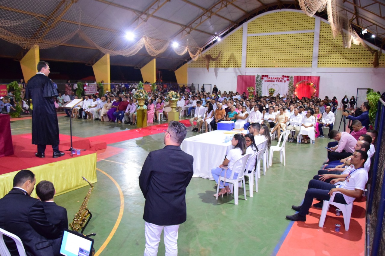 Homens e mulheres, vestidos de branco, sentados em quadra esportiva durante casamento comunitário