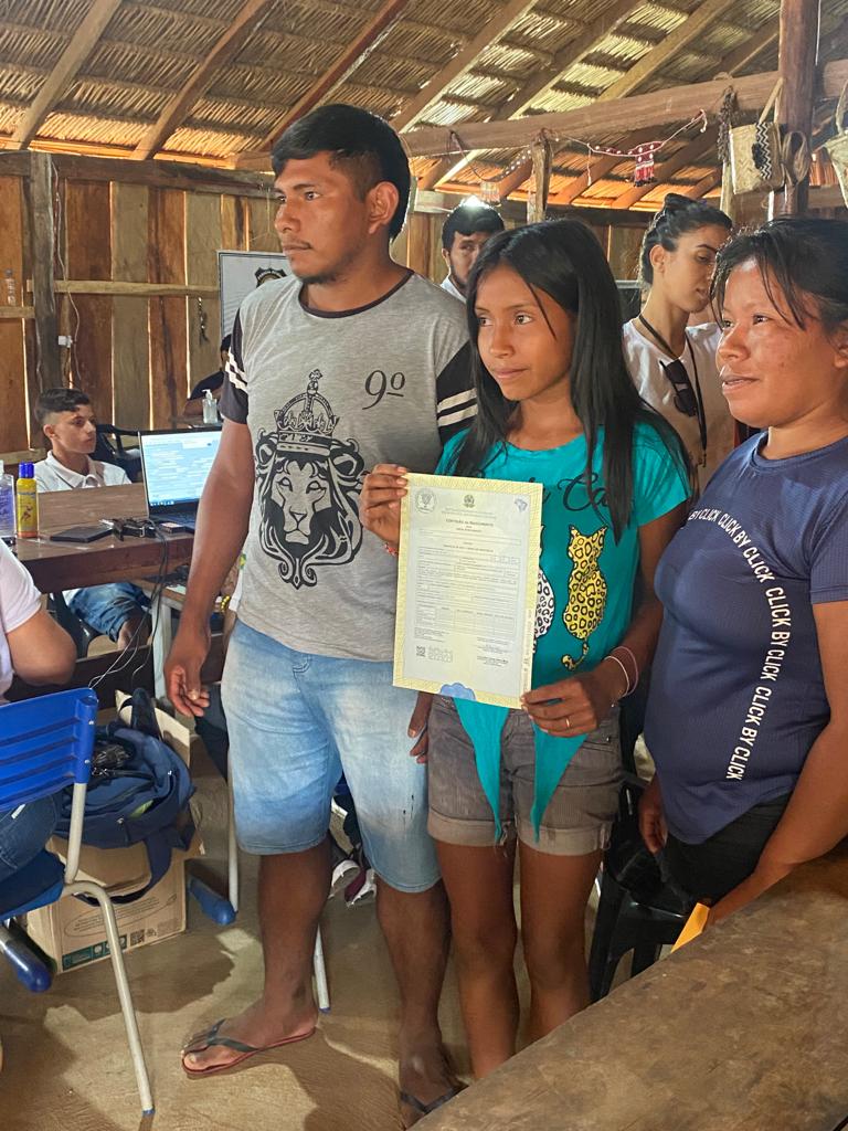 Casal de indígenas com filha adolescente ao meio, com Certidão de Nascimento tardio nas mãos.