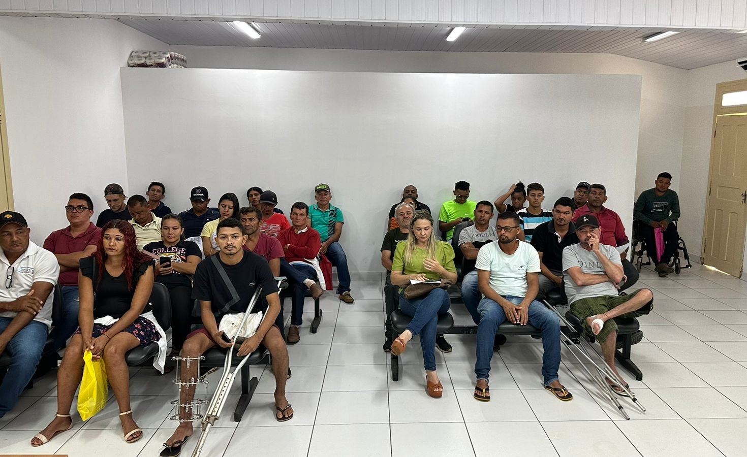 pessoas sentadas em sala de atendimento de chão e paredes brancas.