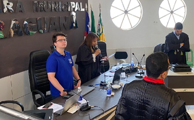 imagem na qual aparecem quatro pessoas, em pé, em uma sala de julgamento, com uma mulher lendo um documento