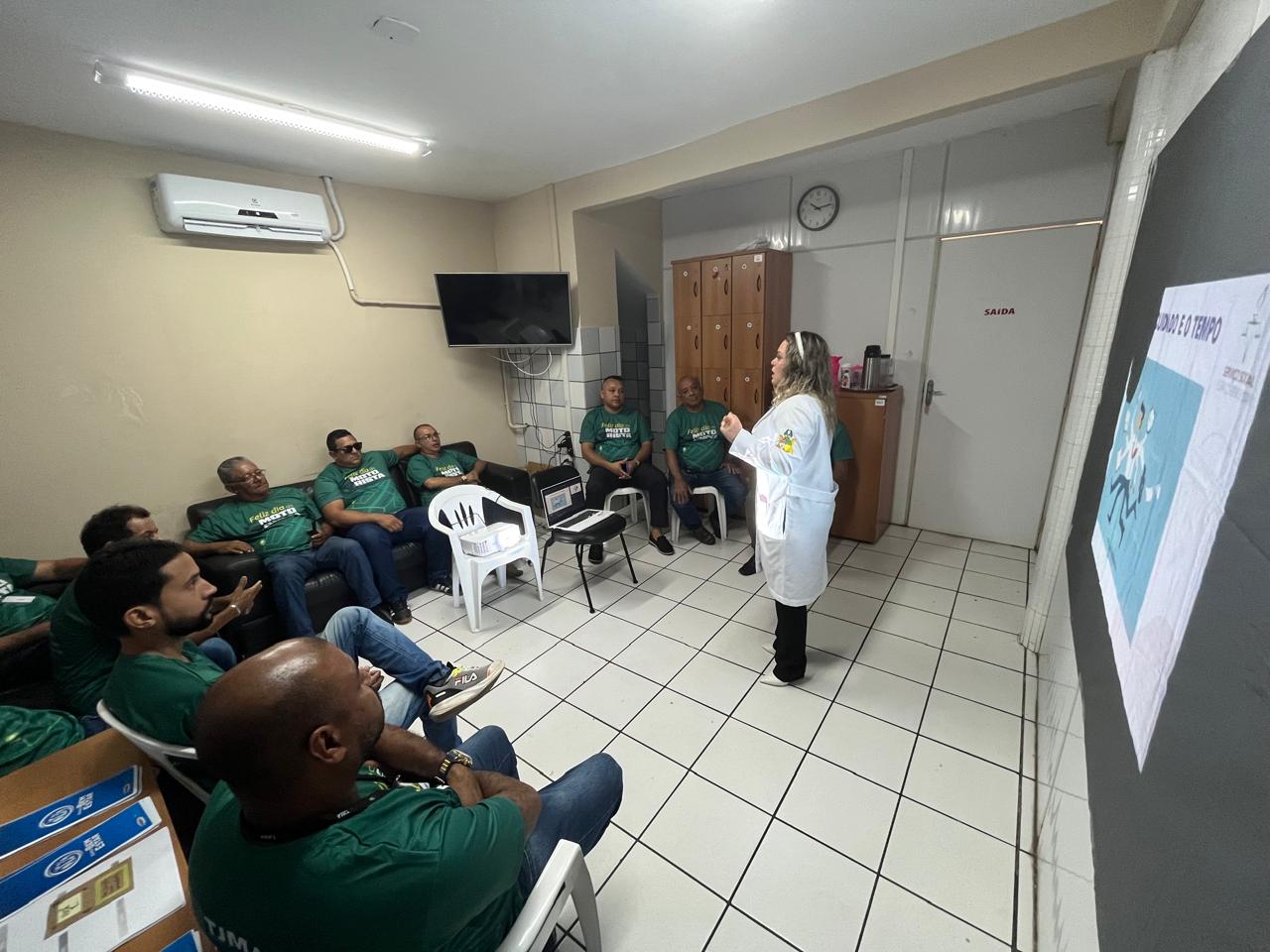 PESSOAS ESTÃO REUNIDAS EM UMA SALA. UMA ASSISTENTE SOCIAL ESTÁ FALANDO. COM UM PROJETOR DE IMAGENS.