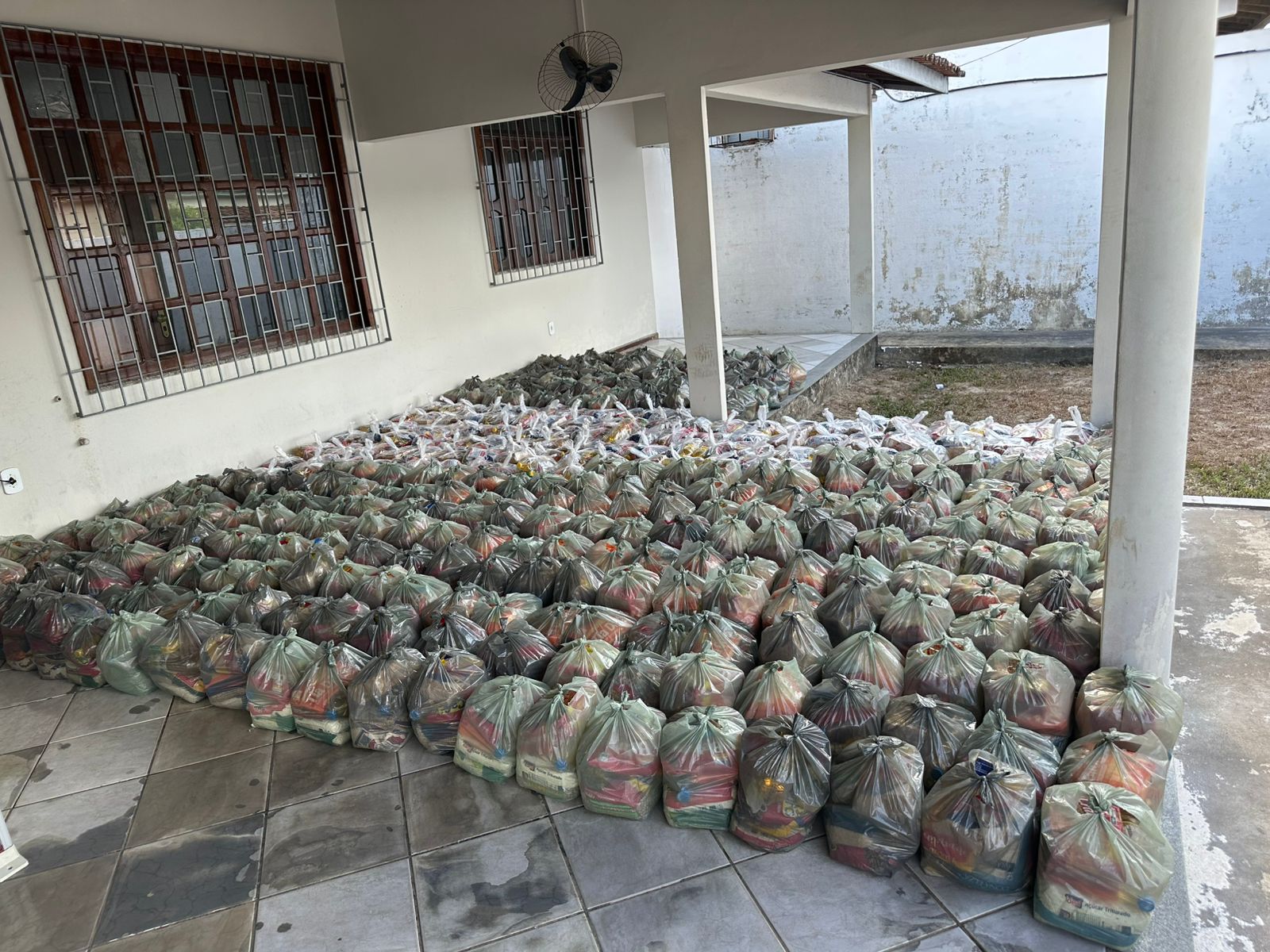 CESTAS BÁSICAS AGRUPADAS NO CHÃO DO FÓRUM DA CIDADE DE BACURI AGRUPADAS EM SACOLAS BRANCAS E CINZAS.