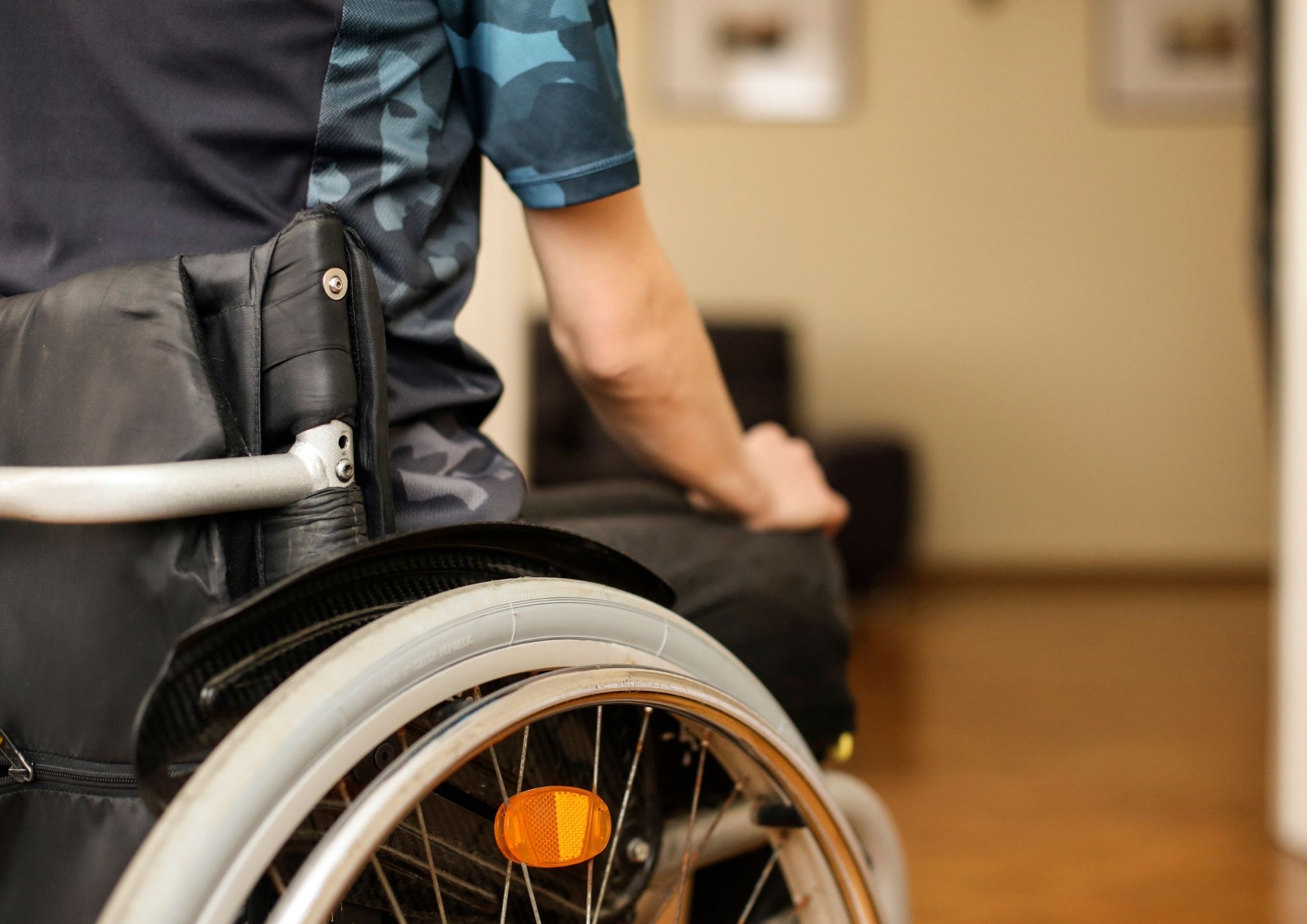 Foto colorida mostra pessoa em cadeira de rodas, seguindo em direção à porta de um cômodo.