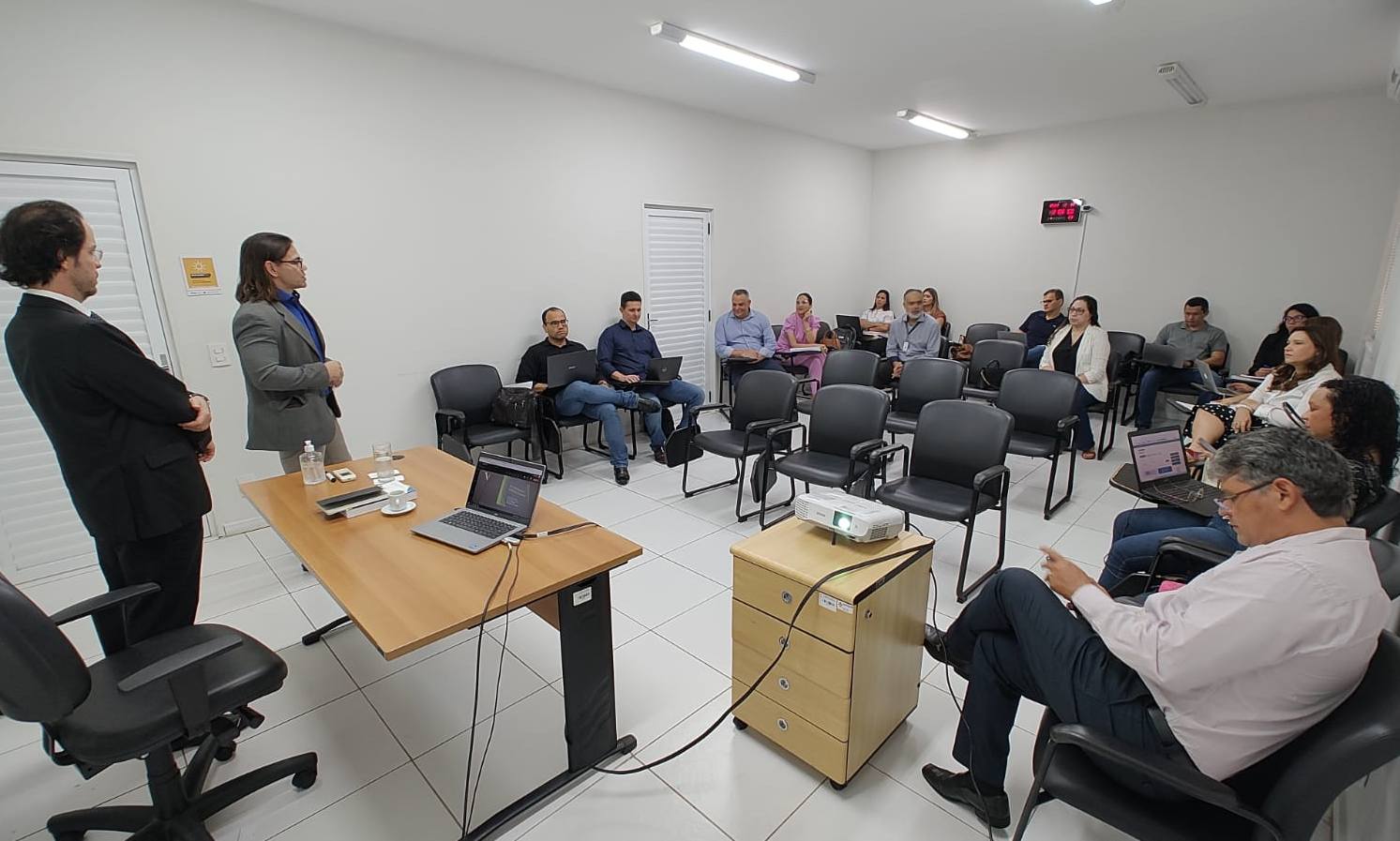 foto retangular da sala da esmam durante aula inaugural do curso de mestrado. sala com paredes e teto brancos, pé direito baixo. alunas e alunos sentados, à frente da turma o secretário da esmam, amudsen bonifácio, e o professor marciano godoy passam as orientações iniciais aos cursistas.