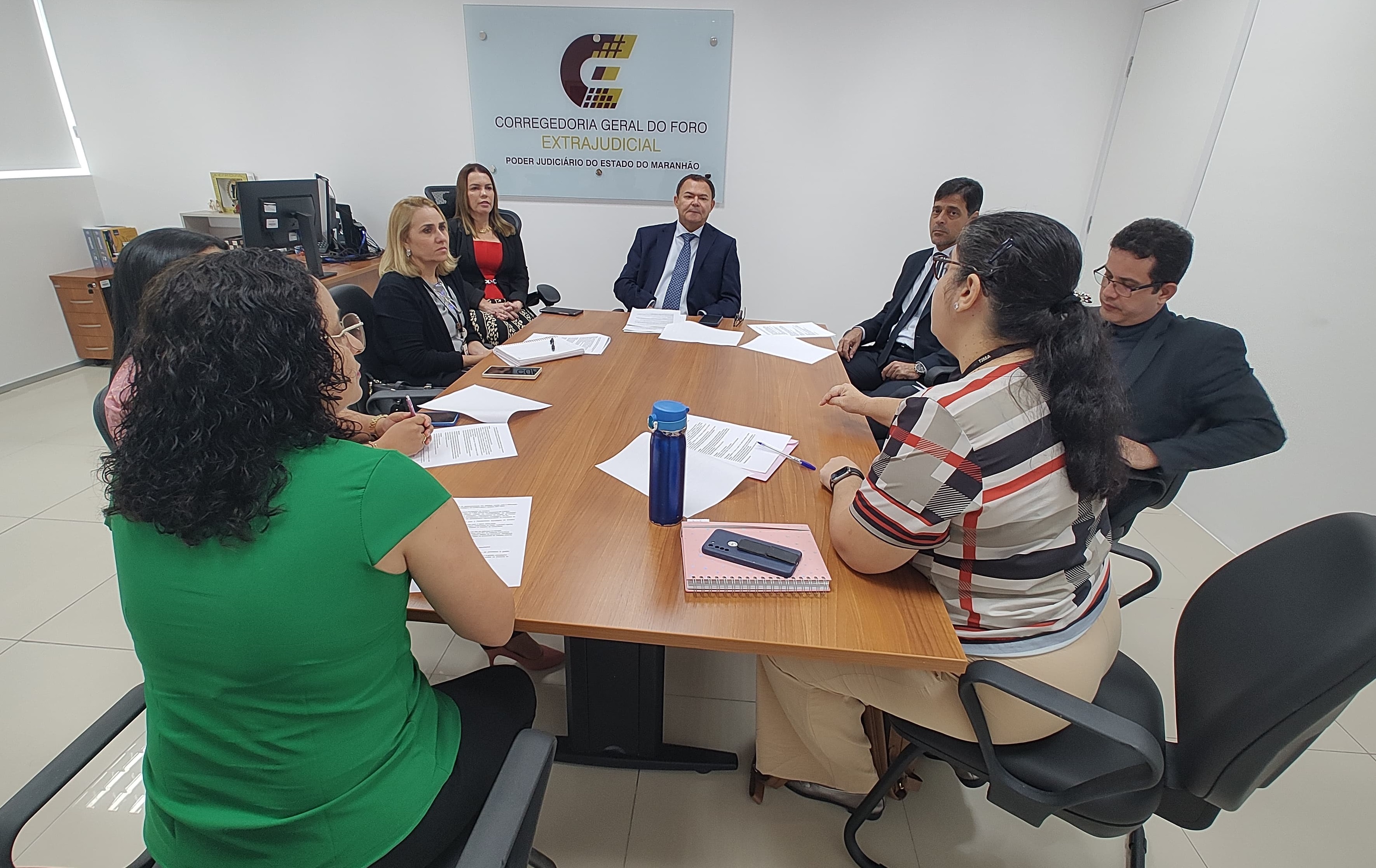 Reunião com a Diretoria de Auditoria Interna do TJMA, realizada na sede da COGEX. Mostram integrantes da Diretoria e da corregedoria extrajudicial em torno de uma mesa de trabalhos, para tratar da continuidade da consultoria para desenvolver o planejamento estratégico da COGEX. Na imagem aparece uma mesa de trabalho marrom, cadeiras pretas e paredes brancas e uma estação de trabalho ao fundo.