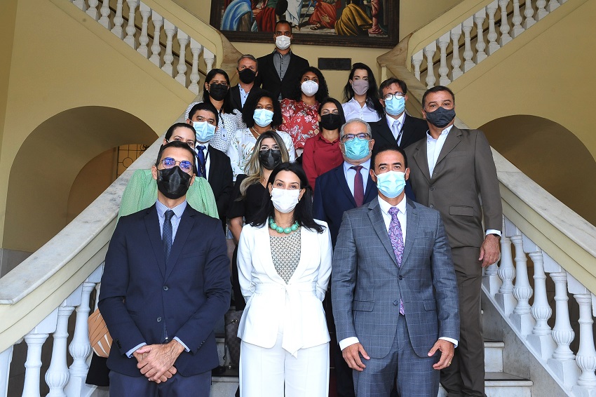 Fotografia colorida. Grupo de pessoas de pé lado a lado, distribuídos nos degraus de escadaria do TJMA, com representantes do TJMA e CNJ. Todos usam máscaras faciais de proteção.