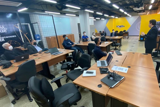 Imagem colorida. Pessoas em uma sala de reunião no Toada Lab.