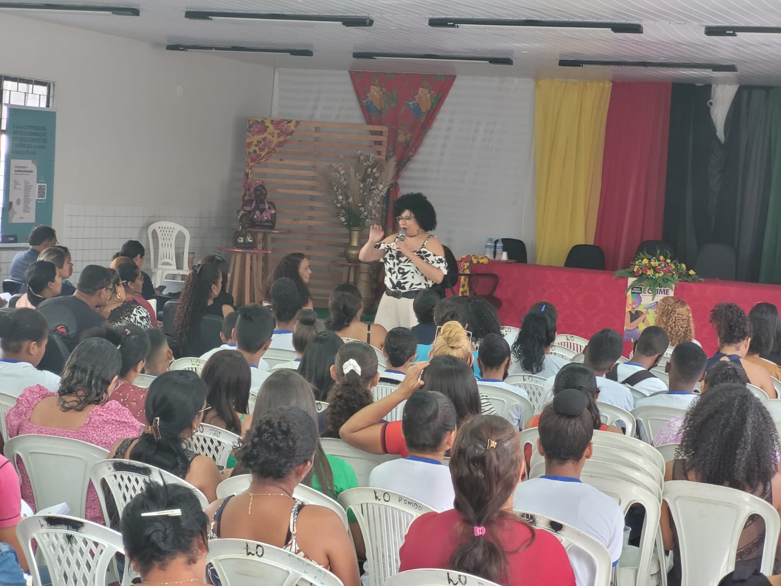 Foto colorida. Pessoas sentadas durante palestra da professora Nila Bastos, em São Luiz Gonzaga, durante ação itinerante do Comitê de Diversidade.