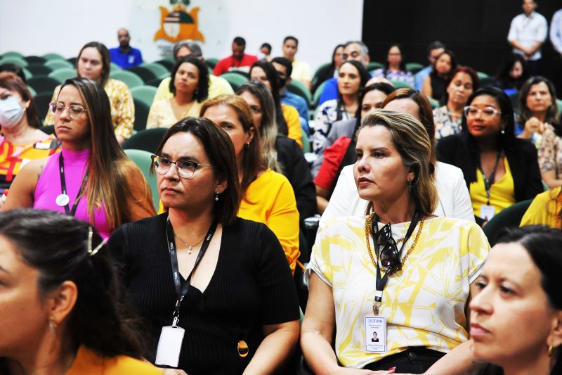 Foto colorida de pessoas sentadas durante palestra no auditório.