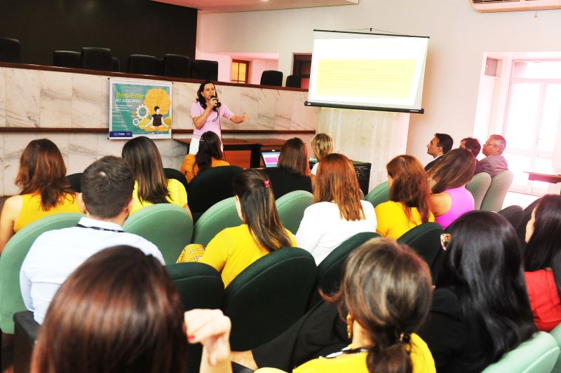 Foto colorida da psiquiatra Talita Serra falando ao microfone durante a palestra ao público.